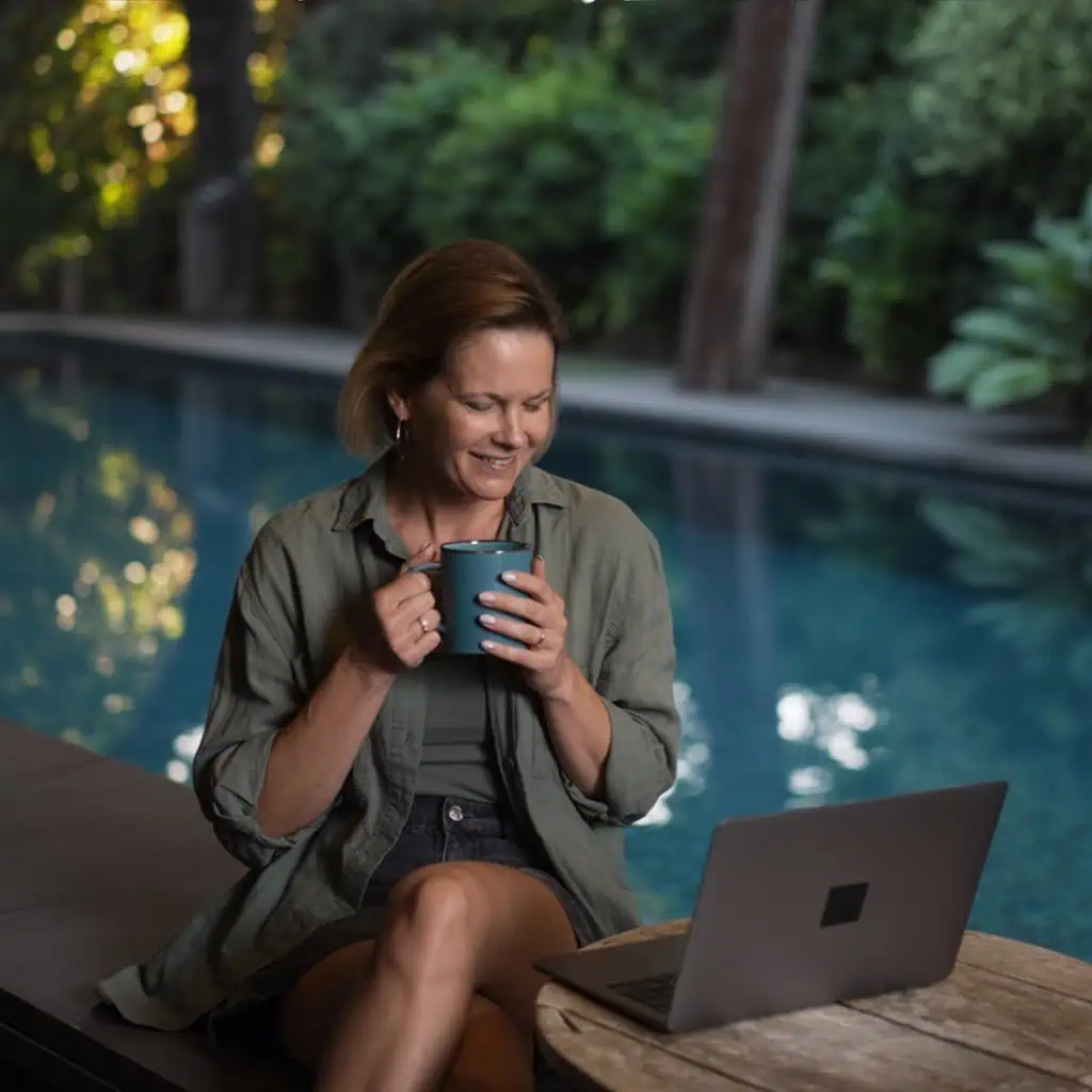 AI generated image of Pam with a cup of coffee working by the pool.